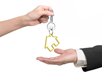 Woman hand giving silver key with golden house shape keyring to man hand, isolated on white background.